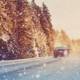 car driving down road with snow with forest