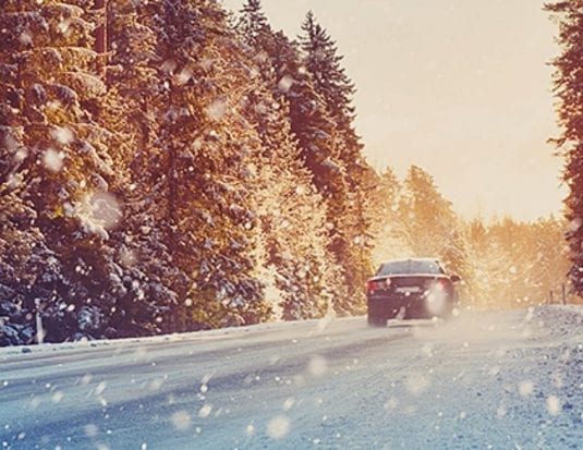car driving down road with snow with forest