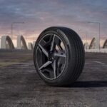 Un pneu Hankook Dynapro Evo AS monté sur une jante moderne noire et argentée, positionné sur une route asphaltée avec un pont et un ciel au crépuscule en arrière-plan.