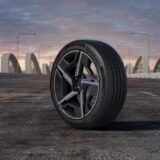 A Hankook Dynapro Evo AS tire mounted on a modern black and silver rim, positioned on an asphalt road with a bridge and twilight sky in the background.