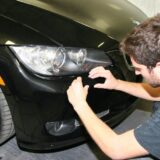 A technician in a black t-shirt performs a cosmetic repair on the front bumper of a black BMW.