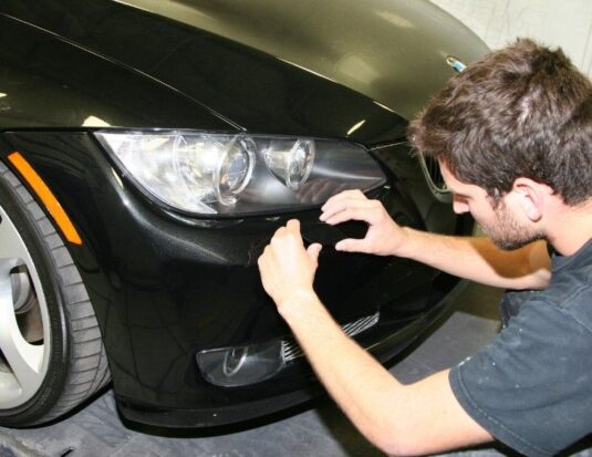 A technician in a black t-shirt performs a cosmetic repair on the front bumper of a black BMW.