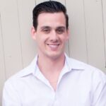 Headshot of J.R. Martino, Vice President and Managing Partner at Budds’ Collision Services, wearing a white collared shirt and smiling against a neutral paneled background.