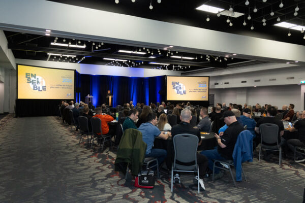 Vue de la salle de conférence lors du 43e colloque annuel d'Auto Prévention au Centre des congrès Delta Trois-Rivières. Environ 140 participants sont réunis autour de tables rondes pour écouter une présentation. Sur scène, deux écrans géants affichent le thème de l'événement : « Ensemble pour un milieu de travail plus sain et plus sécuritaire ».