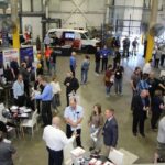 Une vue en plongée d’un salon de pièces automobiles animé dans un entrepôt, illustrant le réseautage entre les participants et des kiosques de fabricants comme Bestbuy.