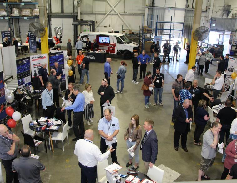 Une vue en plongée d’un salon de pièces automobiles animé dans un entrepôt, illustrant le réseautage entre les participants et des kiosques de fabricants comme Bestbuy.
