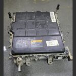 Chargeur embarqué (OBC) d'un Kia Niro EV posé au sol, montrant le boîtier métallique noir et les connecteurs de haute tension.