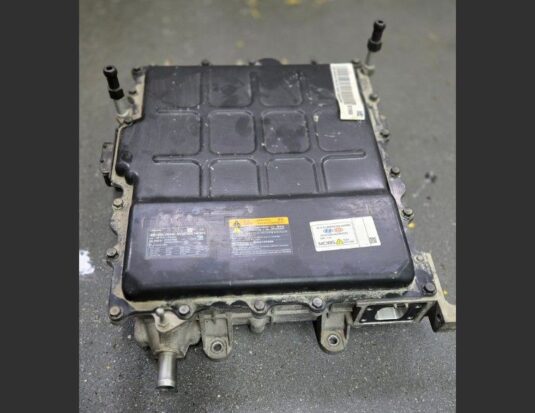Chargeur embarqué (OBC) d'un Kia Niro EV posé au sol, montrant le boîtier métallique noir et les connecteurs de haute tension.