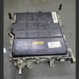A Kia Niro EV onboard battery charger (OBC) module removed from the vehicle, featuring a black metal housing, technical labels, and high-voltage warning stickers.