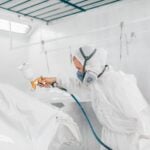 Technicien en carrosserie utilisant un pistolet à peinture dans une cabine de pulvérisation.