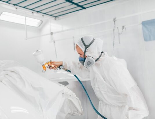 Technicien en carrosserie utilisant un pistolet à peinture dans une cabine de pulvérisation.