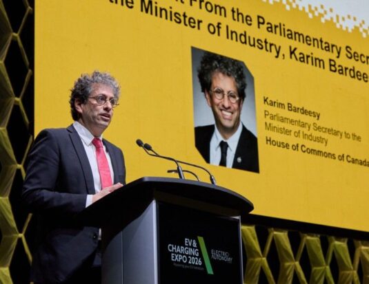 Karim Bardeesy, secrétaire parlementaire du ministre de l'Industrie, prononce un discours au podium lors de l'EV & Charging Expo 2026. Il se tient devant un grand écran jaune qui affiche son portrait, son nom et ses titres officiels auprès de la Chambre des communes du Canada. Le podium porte le logo de l'événement « EV & Charging Expo 2026 ». Lors de cette allocution, M. Bardeesy a annoncé un investissement fédéral de 10,6 millions de dollars pour financer 14 projets d'infrastructure de recharge de véhicules électriques à travers le pays.