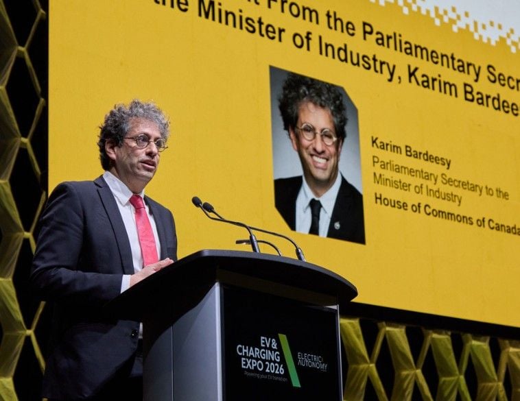 Karim Bardeesy, secrétaire parlementaire du ministre de l'Industrie, prononce un discours au podium lors de l'EV & Charging Expo 2026. Il se tient devant un grand écran jaune qui affiche son portrait, son nom et ses titres officiels auprès de la Chambre des communes du Canada. Le podium porte le logo de l'événement « EV & Charging Expo 2026 ». Lors de cette allocution, M. Bardeesy a annoncé un investissement fédéral de 10,6 millions de dollars pour financer 14 projets d'infrastructure de recharge de véhicules électriques à travers le pays.