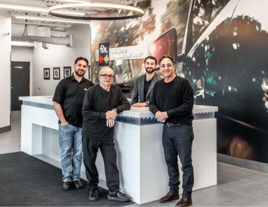 The Rosanova family (Max, Otto, Mike, and Albert) standing behind the modern white reception desk at on of their Fix Auto shops.