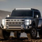 Front three-quarter view of the silver Hyundai Boulder Concept, a rugged body-on-frame SUV. The vehicle features an upright "Art of Steel" design , large 37-inch mud-terrain tires , vertical LED headlight stacks, and a roof-mounted light bar, positioned on rocky terrain.