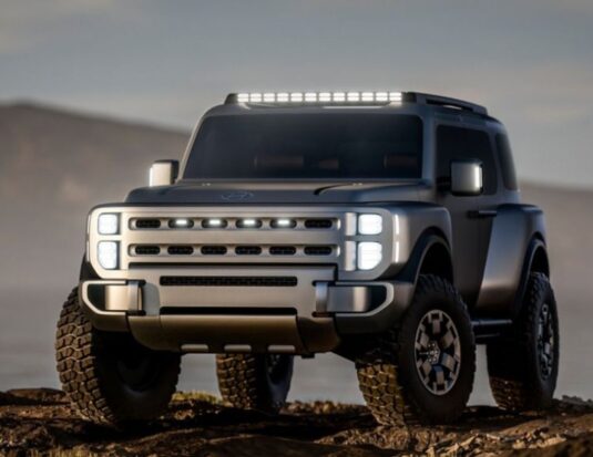 Front three-quarter view of the silver Hyundai Boulder Concept, a rugged body-on-frame SUV. The vehicle features an upright "Art of Steel" design , large 37-inch mud-terrain tires , vertical LED headlight stacks, and a roof-mounted light bar, positioned on rocky terrain.