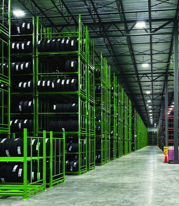 A vast warehouse interior featuring long rows of tall green metal racks filled with tires, illustrating Unimax's strategic investments to enhance storage capacity and product availability.