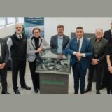 Eight professionals from the Ontario Vehicle Innovation Network (OVIN) and Schaeffler stand around a display case of mechanical components to mark their strategic partnership.