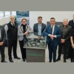 Huit professionnels du Réseau ontarien d’innovation pour les véhicules (ROIV) et de Schaeffler se tiennent autour d'une vitrine d'exposition remplie de pièces mécaniques pour souligner leur partenariat stratégique.