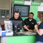 Deux conseillers techniques derrière un comptoir de service accueillent une cliente. Cette scène illustre l'importance cruciale des 10 premières minutes pour bâtir la confiance et apaiser l'incertitude des clients dès leur arrivée à l'atelier.
