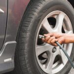 Un gros plan d'une personne utilisant un tuyau d'air comprimé pour vérifier la pression ou gonfler le pneu d'une voiture grise sur une jante en alliage.