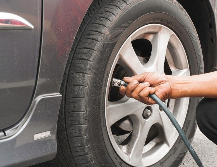 Un gros plan d'une personne utilisant un tuyau d'air comprimé pour vérifier la pression ou gonfler le pneu d'une voiture grise sur une jante en alliage.