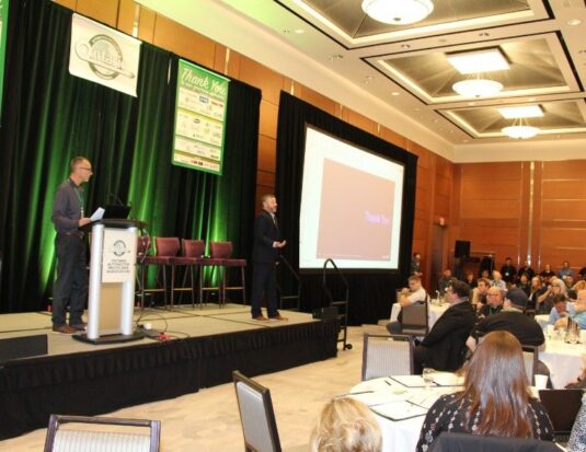 A speaker stands on a stage with a podium and large screen during a presentation at the OARA Convention 2026, where over 430 attendees gathered for the association's best-attended event on record.