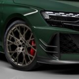 Close-up of a dark green Audi RS 3 competition limited featuring a bronze multi-spoke alloy wheel, red Audi ceramic brake calipers, and Pirelli P Zero Trofeo R tires. The image highlights the carbon fiber aero canards and modern LED headlight design.