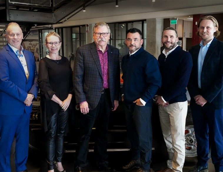 A group of six professionally dressed people from PBS Systems and Dealer Image Pro standing side-by-side in a modern automotive showroom, posing together to commemorate their partnership.