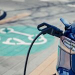 Gros plan sur l'arrière d'un véhicule électrique bleu en train de se recharger, avec un câble branché dans la prise et un symbole de stationnement pour voiture électrique peint en vert sur le sol en arrière-plan.