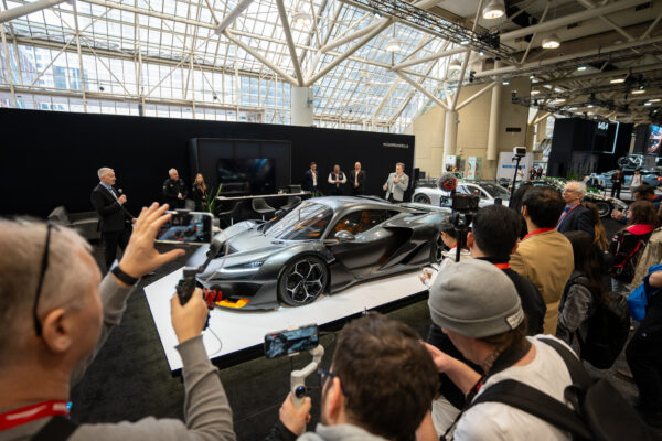 La supervoiture McLaren W1 grise sur une plateforme d'exposition blanche lors de ses débuts nord-américains au Salon international de l’auto du Canada 2026 , entourée d’une foule de visiteurs et de photographes sous le plafond de verre du Metro Toronto Convention Centre.  