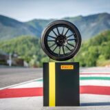 A Pirelli P Zero Trofeo RS tire on a black rim, displayed on a pedestal at a race track with green mountains in the background.