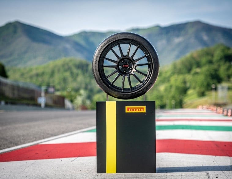 A Pirelli P Zero Trofeo RS tire on a black rim, displayed on a pedestal at a race track with green mountains in the background.