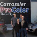 Quatre personnes souriantes, les nouveaux propriétaires, posant devant l'enseigne « Carrossier ProColor Shawinigan » fixée sur un mur de métal noir.