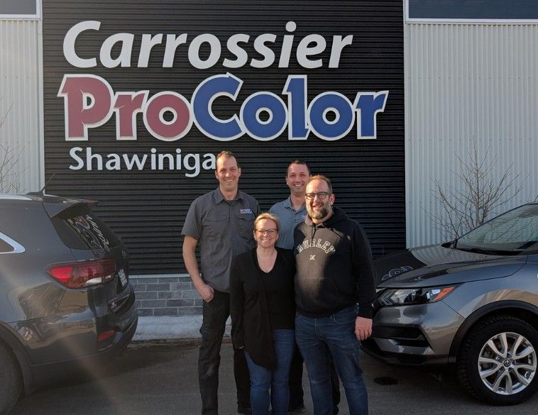 Quatre personnes souriantes, les nouveaux propriétaires, posant devant l'enseigne « Carrossier ProColor Shawinigan » fixée sur un mur de métal noir.