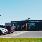Vue extérieure d'une station de recharge Plug Inn du Groupe Renault, un bâtiment modulaire noir affichant « CHARGE RAPIDE TOUTES MARQUES ». Plusieurs voitures électriques, dont des modèles Renault et Alpine, sont garées devant.