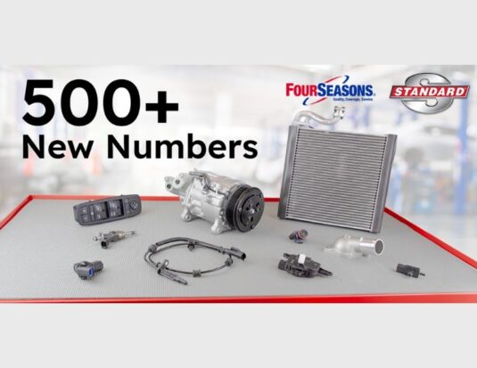 Image promotionnelle de Standard Motor Products pour le lancement de son T1 2026, avec le texte « 500+ Nouveaux Numéros » et les logos de Four Seasons et Standard. L'image présente diverses pièces automobiles, dont un compresseur de climatisation, un radiateur, un commutateur de lève-vitre électrique et un câble de capteur ABS. Les pièces sont disposées sur un établi d'atelier.