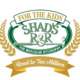 A charity logo with gold and green elements. An upper gold banner reads "FOR THE KIDS". A large green oval frames "SHAD'S R&R" with a crossed golf club and the text "FOR MUSCULAR DYSTROPHY". Gold wheat stalks frame the sides, and a lower gold banner reads "Road to Ten Million".