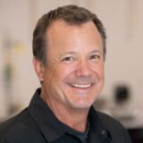 A headshot of Shawn Collins, the new Training Director for Pro Spot International, smiling and wearing a black collared shirt against a blurred background.