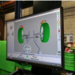 Écran d'ordinateur dans un atelier de service automobile affichant une interface numérique de diagnostic d'alignement des roues avec un graphique 3D des pneus et de l'essieu d'un véhicule.
