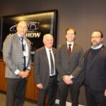 Quatre personnes, Huw Williams, David Adams, Brian Kingston et Flavio Volpe, posent côte à côte lors d’une conférence de presse au Salon international de l’auto du Canada en 2026. En arrière-plan, un grand écran affiche le logo « AUTO SHOW » avec la silhouette d'une voiture.