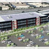 Artist’s rendering of a modern, three-story Toyota facility featuring solar panels on the roof, a large parking lot with numerous cars, and landscaped greenery. The building displays black and red architectural accents with a visible "TOYOTA" sign at the entrance.