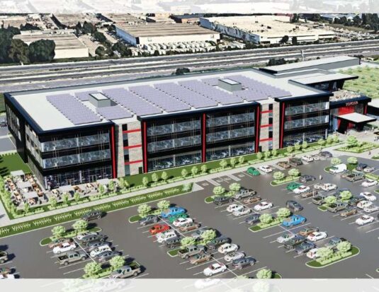 Illustration architecturale d'un bâtiment moderne de trois étages de Toyota, doté de panneaux solaires sur le toit, d'un grand stationnement rempli de véhicules et d'aménagements paysagers verdoyants. Le design extérieur arbore des accents noirs et rouges avec une enseigne « TOYOTA » visible à l'entrée.