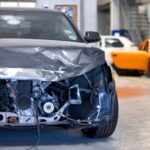 Vue avant d'une voiture grise gravement endommagée dans un atelier de carrosserie, exposant les composants internes du moteur et de la structure.