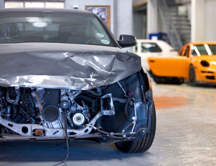 Vue avant d'une voiture grise gravement endommagée dans un atelier de carrosserie, exposant les composants internes du moteur et de la structure.