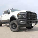 Low-angle front view of a white 2026 RAM 2500 Power Wagon with black grille, off-road tires, and lower body blackout graphics.