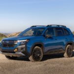 Un Subaru Forester Wilderness hybride 2027 bleu stationné sur un sentier de gravier, mettant en valeur sa garde au sol de 9,3 pouces, ses jantes de 17 pouces noir mat et ses pneus tout-terrain Yokohama Geolandar.