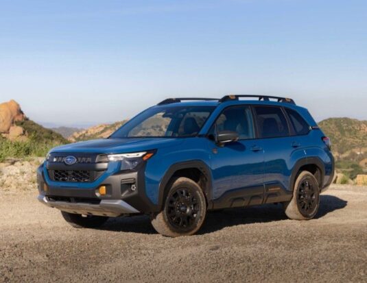 Un Subaru Forester Wilderness hybride 2027 bleu stationné sur un sentier de gravier, mettant en valeur sa garde au sol de 9,3 pouces, ses jantes de 17 pouces noir mat et ses pneus tout-terrain Yokohama Geolandar.