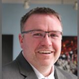 Professional headshot of Josh Wilber, Vice President of Human Resources at Grote Industries, wearing a gray suit and glasses, smiling at the camera.