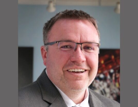 Professional headshot of Josh Wilber, Vice President of Human Resources at Grote Industries, wearing a gray suit and glasses, smiling at the camera.